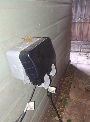 Weatherproof outdoor socket installed beside the garden building.